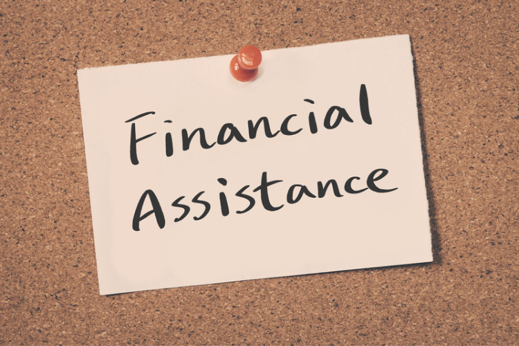 Post-it note stuck to a corkboard that says "Financial Assistance"